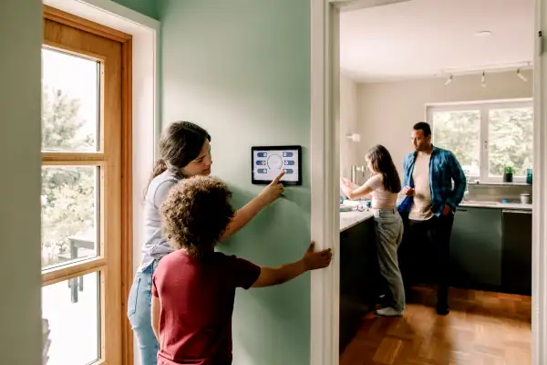 Mother explaining smart home app to son on digital tablet while family in kitchen at home