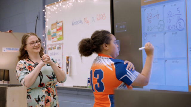 teacher watches student work out math problem
