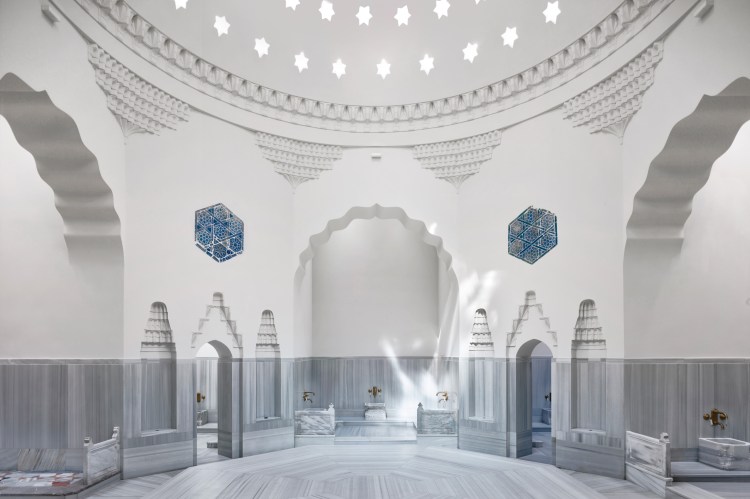Interior of a Turkish bath with marble floors and walls, arched doorways, and star-shaped skylights.