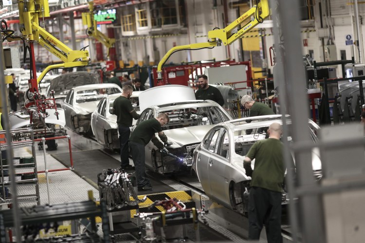 Workers assembling Jaguar XJ automobiles on a production line.