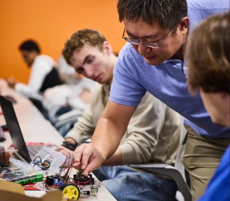 Instructor leaning over student's shoulder giving guidance on an electornical device